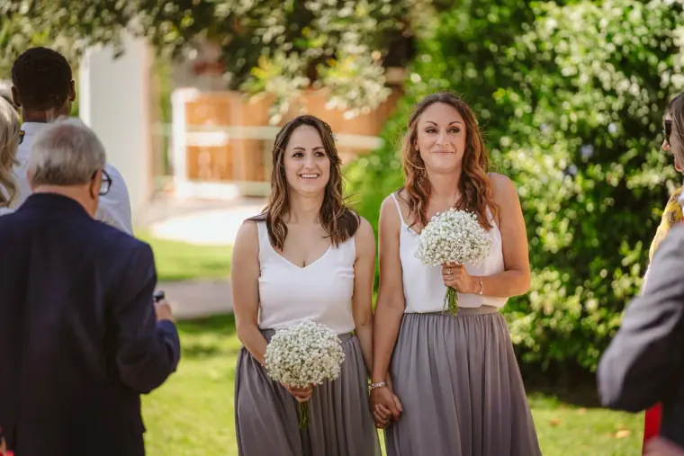 Two bridesmaids in grey skirts holding gypsophila posies before the ceremony