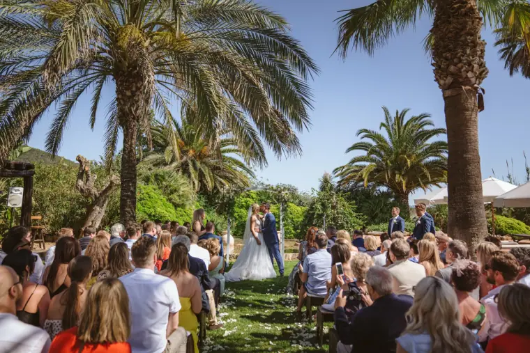Wide view of the ceremony with guests seated beneath tall palm trees at Can Gall, Ibiza