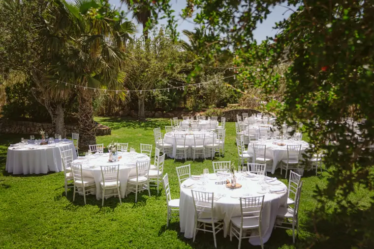 Round tables with white linen and chairs set out on a shady lawn