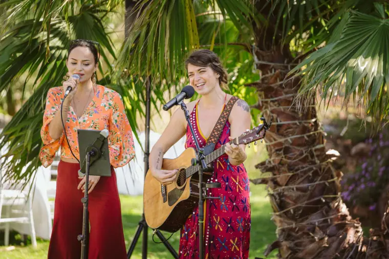 Two singers performing with a guitar beneath palm trees