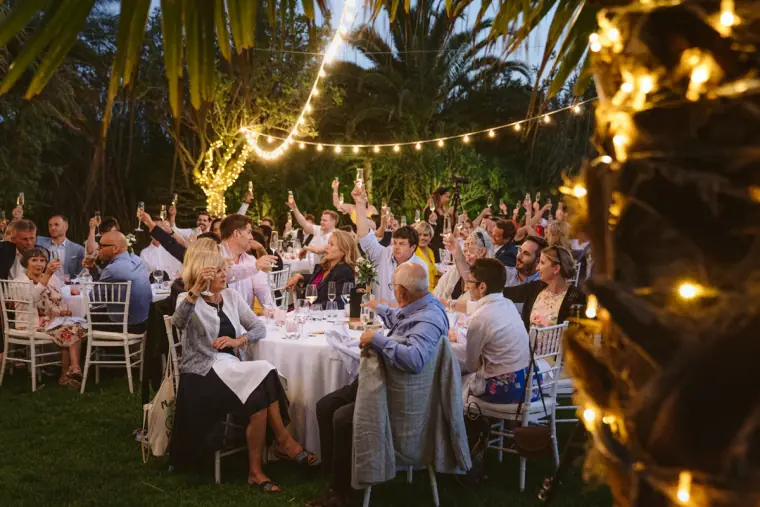 Guests cheering at round tables beneath festoon lights at dusk, Can Gall