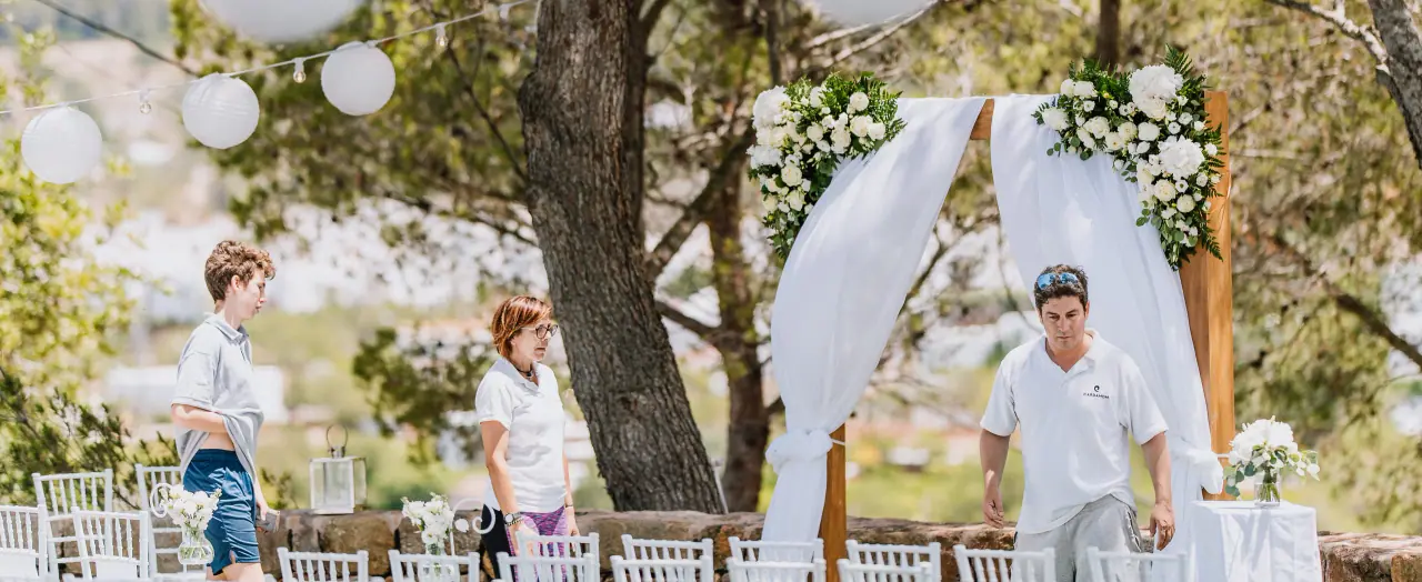 Planners setting up a white draped ceremony arch with flowers and paper lanterns at Can Curreu, Ibiza