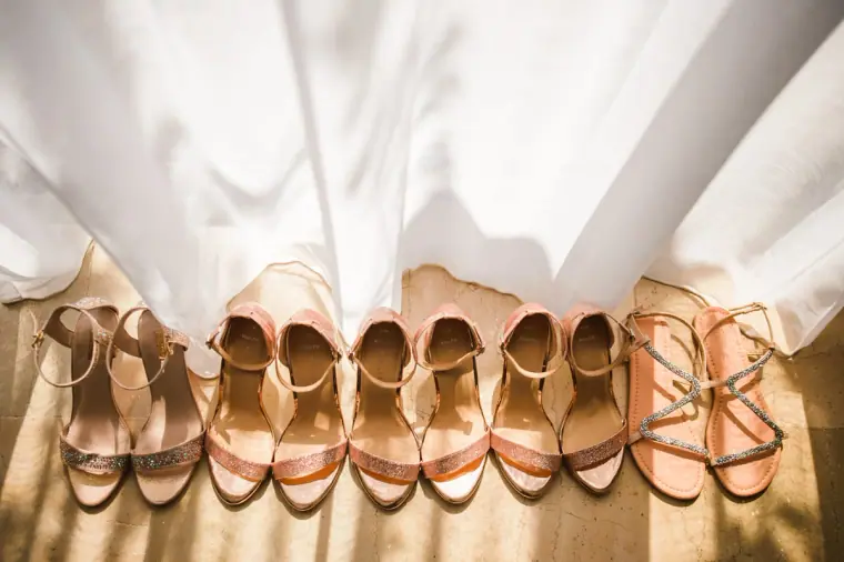 Row of rose-gold bridesmaid sandals lined up beneath white curtains