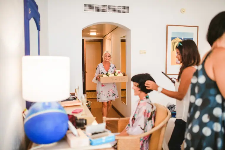Bridal party getting ready in a hotel room as a woman arrives carrying a tray