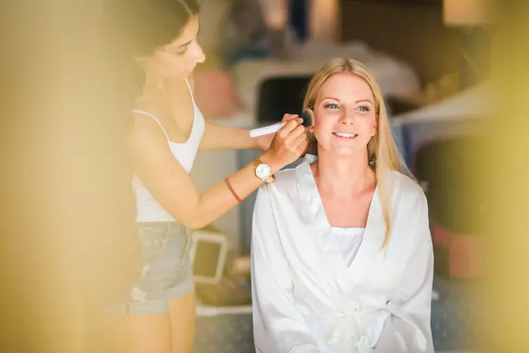 Make-up artist applying make-up to Charlotte, smiling in her white robe