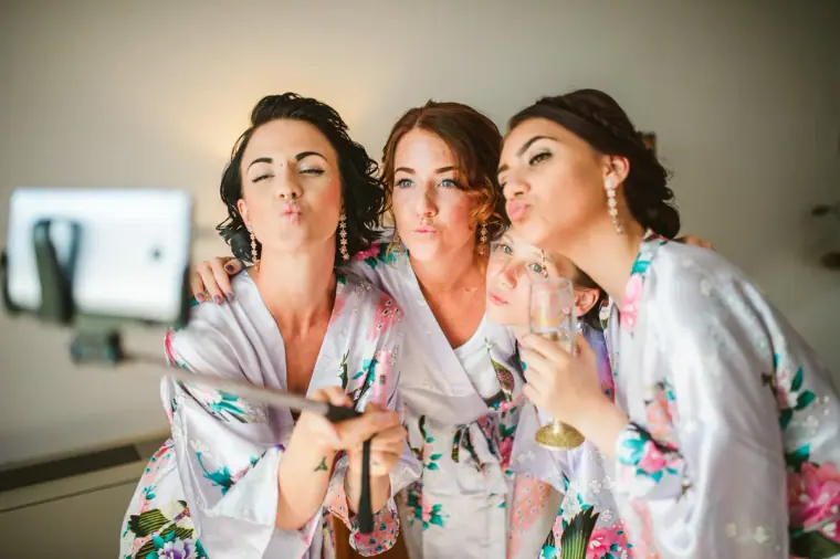 Three bridesmaids in floral robes pulling faces for a selfie stick photo