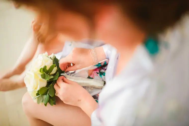 Close-up of hands wrapping a white rose bouquet with ribbon