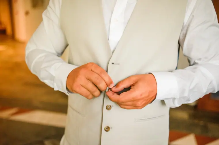 Close-up of the groom buttoning his cream waistcoat
