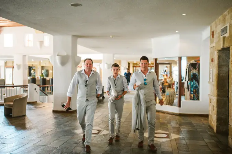 Groom and groomsmen in cream waistcoats walking through the Coral Beach Hotel lobby