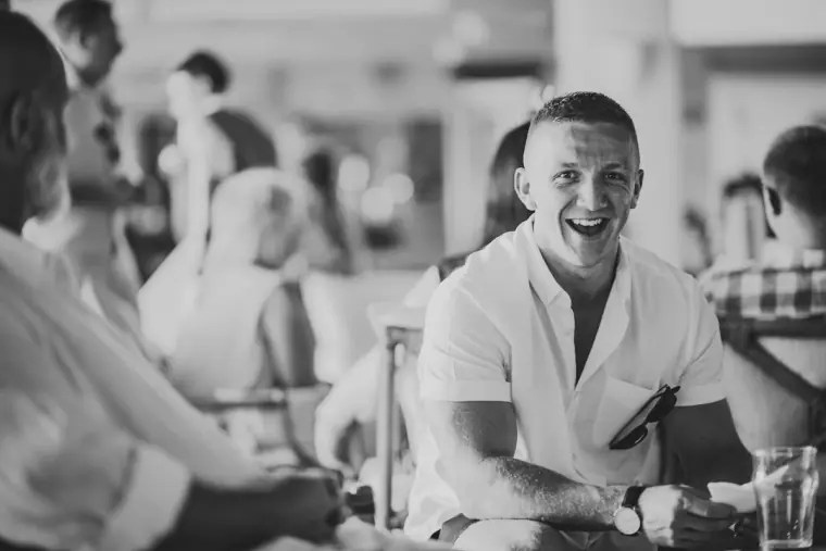 Black-and-white photo of a guest laughing at a table before the ceremony