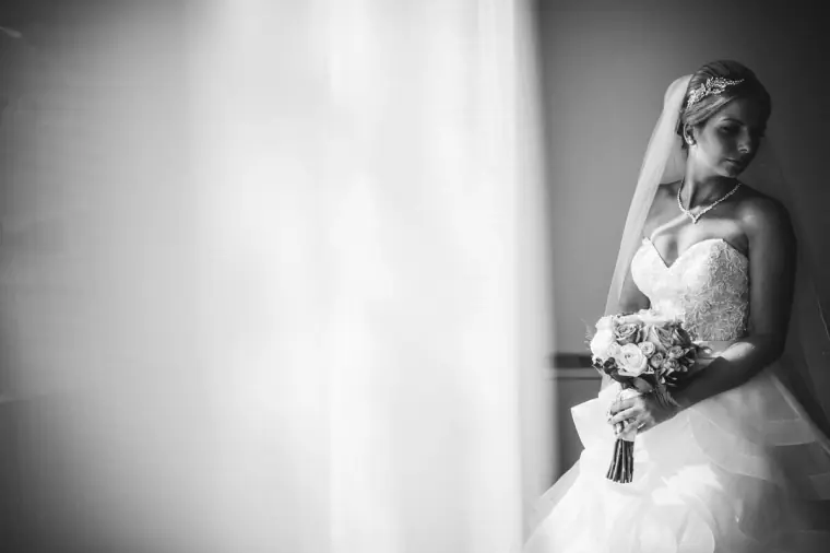 Black-and-white portrait of the bride with veil and bouquet in soft window light