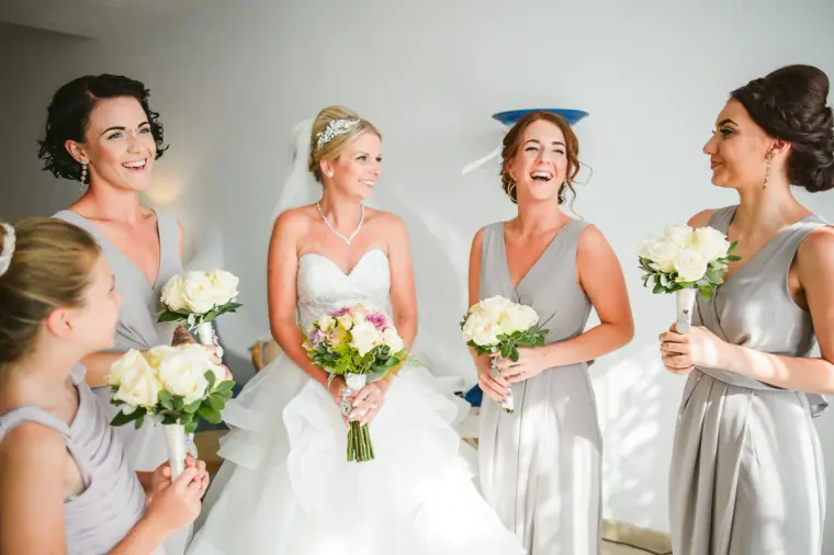 Charlotte laughing with her bridesmaids in grey dresses holding white rose bouquets
