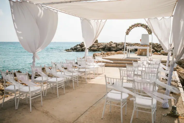 White chairs and draped canopy set for a seaside ceremony at Coral Beach Hotel, Paphos