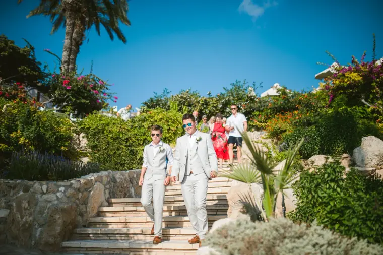 Groom and groomsmen walking down garden steps towards the ceremony at Coral Beach Hotel