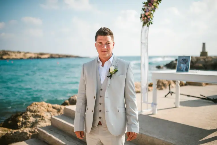 Nathan waiting by the floral arch with the sea behind him at Coral Beach Hotel, Paphos