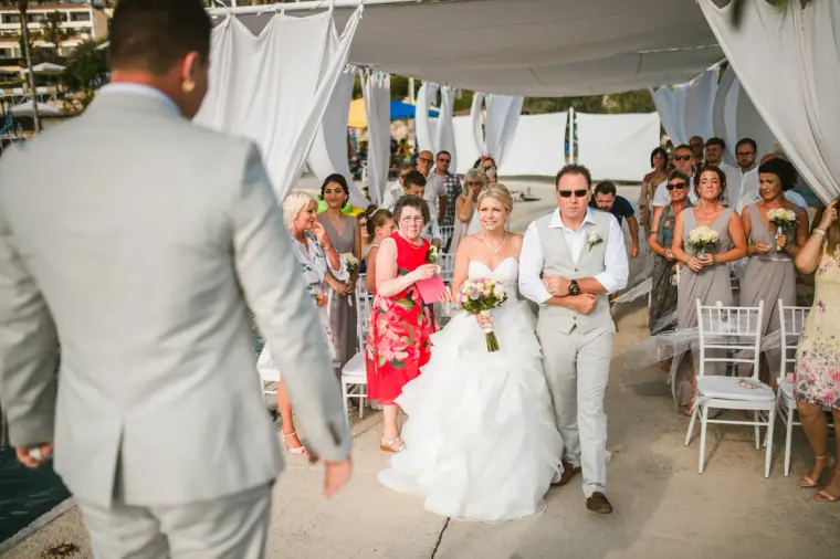 Charlotte walking down the aisle with her father towards Nathan at the seaside ceremony