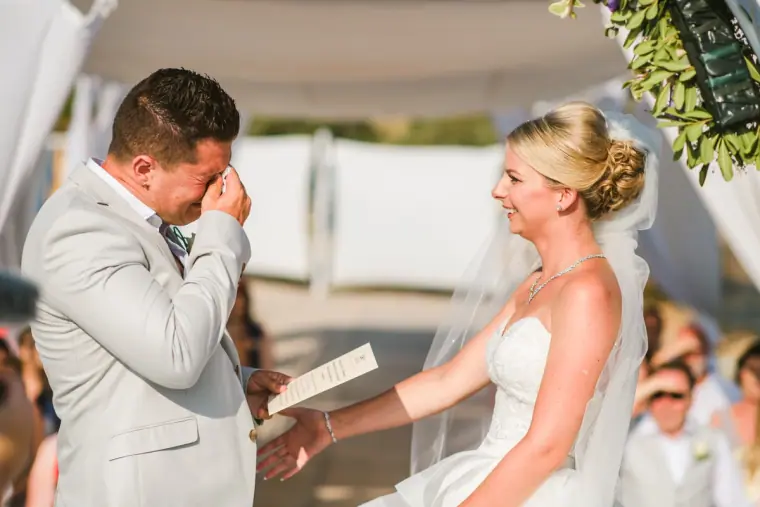 Nathan wiping his eyes as Charlotte reads her vows beneath the white canopy