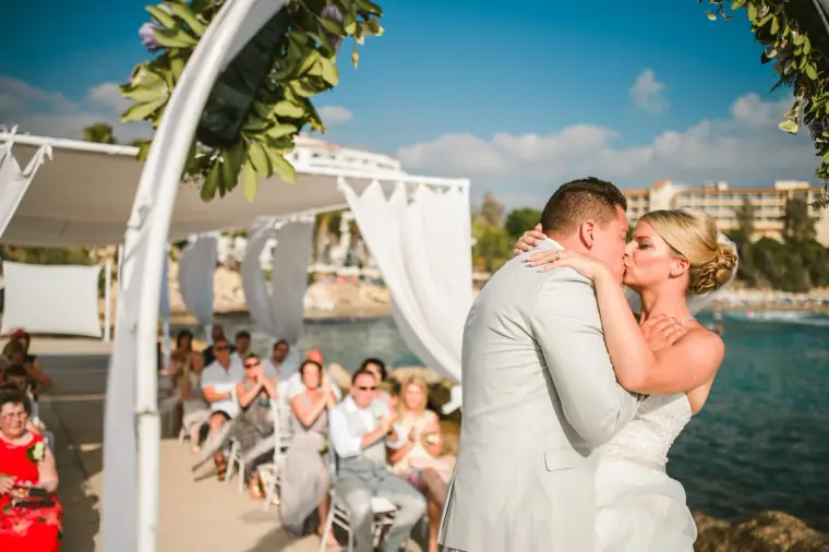 Charlotte and Nathan's first kiss under the arch as guests applaud by the sea
