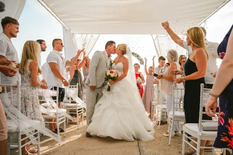 Newlyweds kissing in the aisle as cheering guests celebrate around them