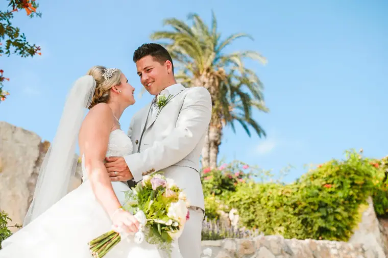 Newlyweds laughing together with palm trees and blue sky behind them