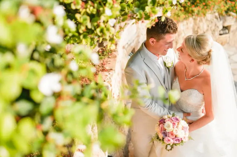 Newlyweds embracing among white flowers and greenery, Coral Beach Hotel, Paphos