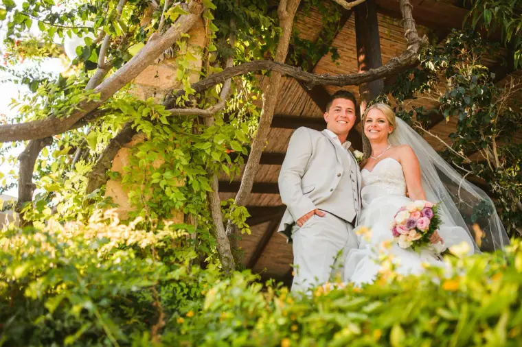Bride and groom under a wooden treehouse in the Coral Beach Hotel gardens