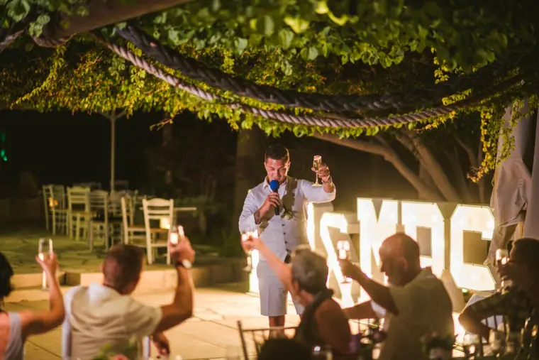 Groom raising his glass during his speech as guests cheer