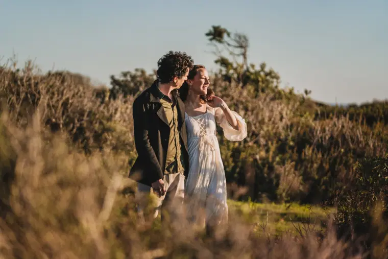 Couple walking hand in hand through golden scrubland above the coast