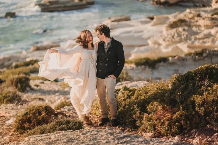 Aiko and Erez laughing together on white limestone rocks by turquoise water