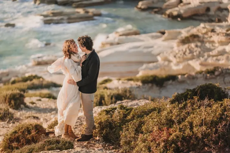 Aiko and Erez embracing on a coastal path above turquoise water at the Paphos sea caves