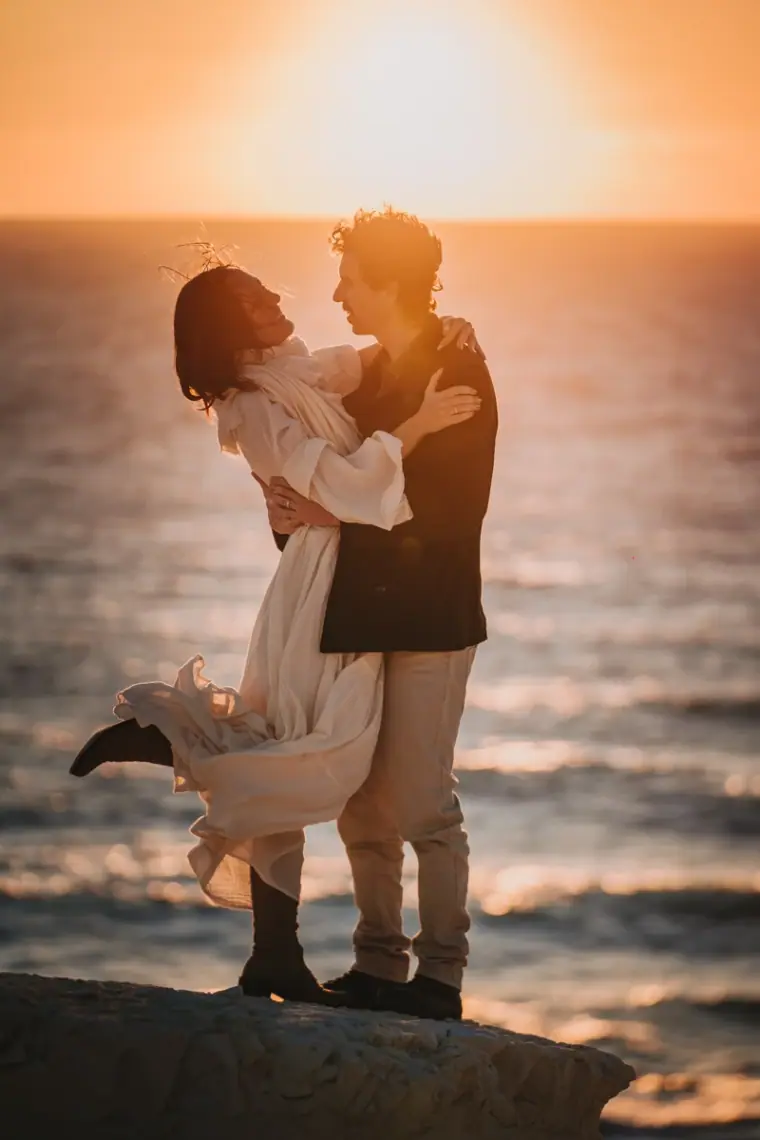Erez lifting Aiko off her feet on the rocks as the sun sets over the sea