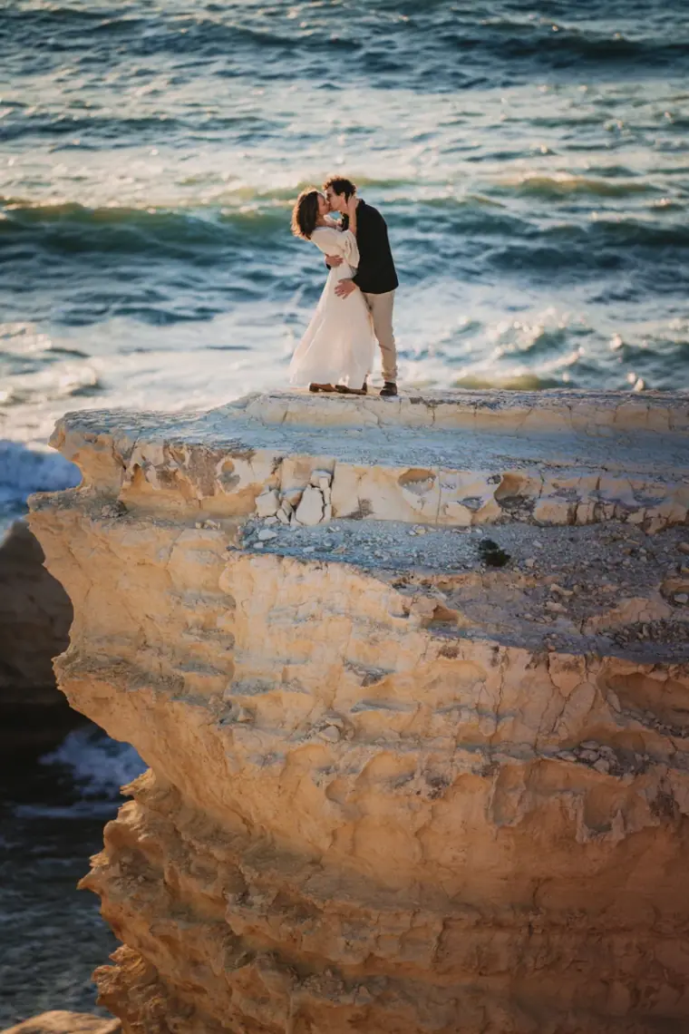 Couple kissing on the edge of a layered limestone sea cliff near Paphos