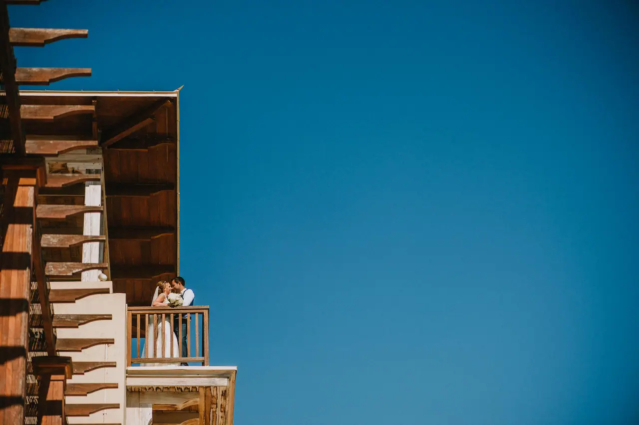 Danielle and Aaron kissing on a wooden balcony against a deep blue sky at Elea Estate, Paphos