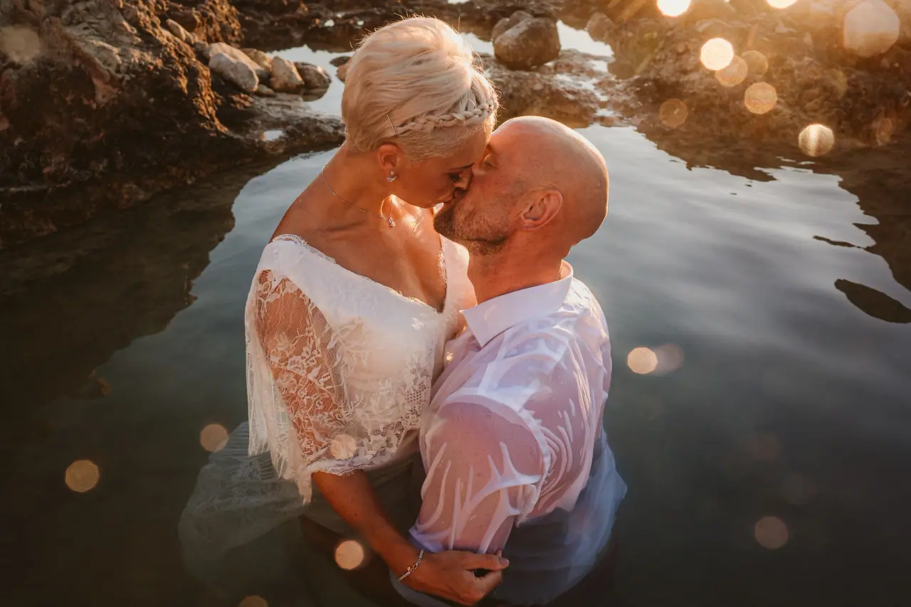 Alana and Luke kissing waist-deep in a glowing rock pool for their trash the dress shoot near Paphos
