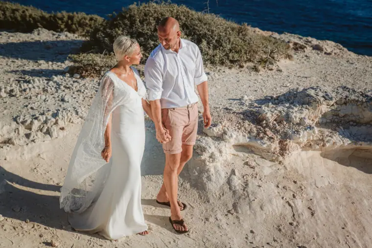 Couple walking hand in hand across white limestone rocks by the coast