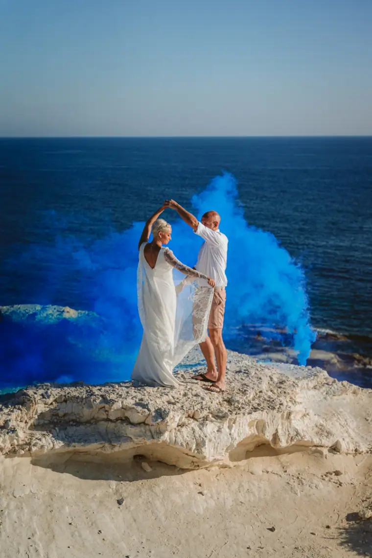 Couple dancing on a clifftop as blue smoke billows against the sea