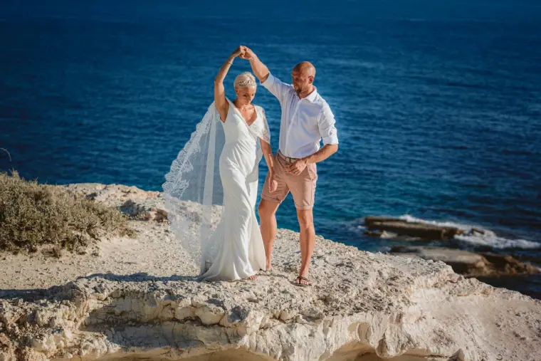 Luke twirling Alana on white rocks above the sea, her lace cape flying