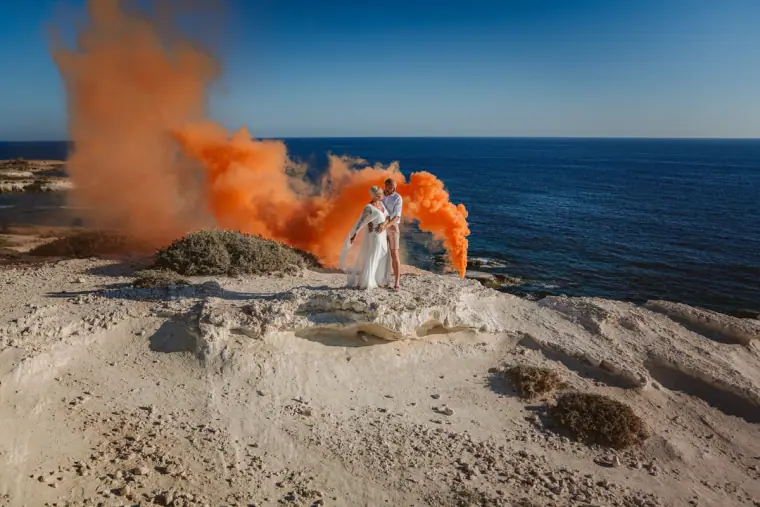 Bright orange smoke flare streaming beside the couple on the Paphos coast