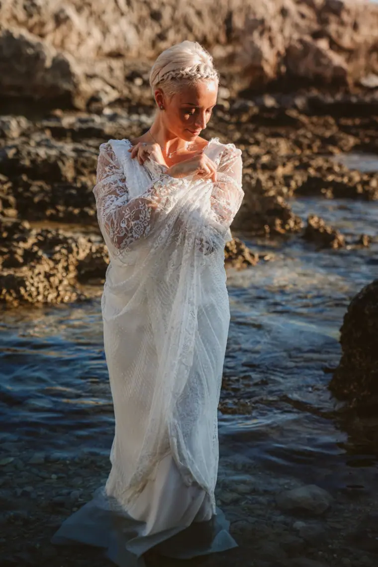 Alana standing in a rock pool in her lace dress, looking down