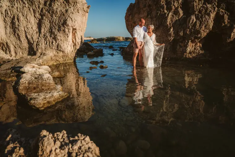 Couple standing in a sea cave rock pool framed by golden rocks near Paphos