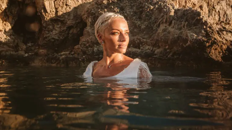 Alana half-submerged in a rock pool in her lace dress, gazing into the light