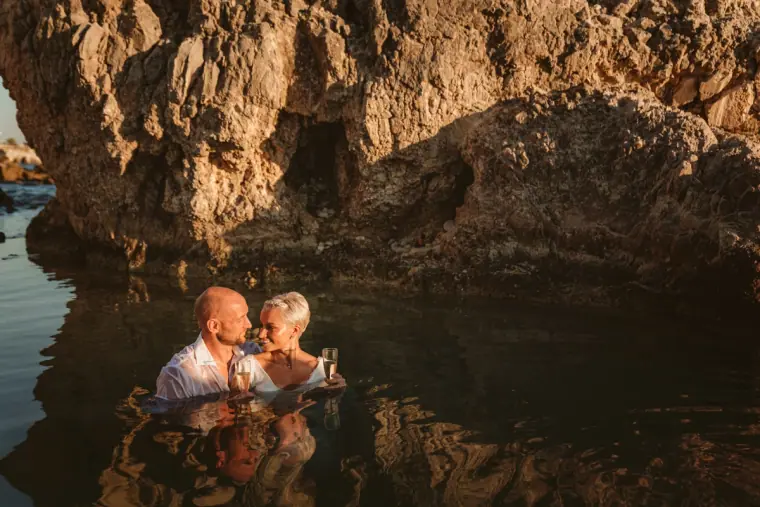 Couple sitting in a sheltered sea cave pool beneath towering rocks near Paphos