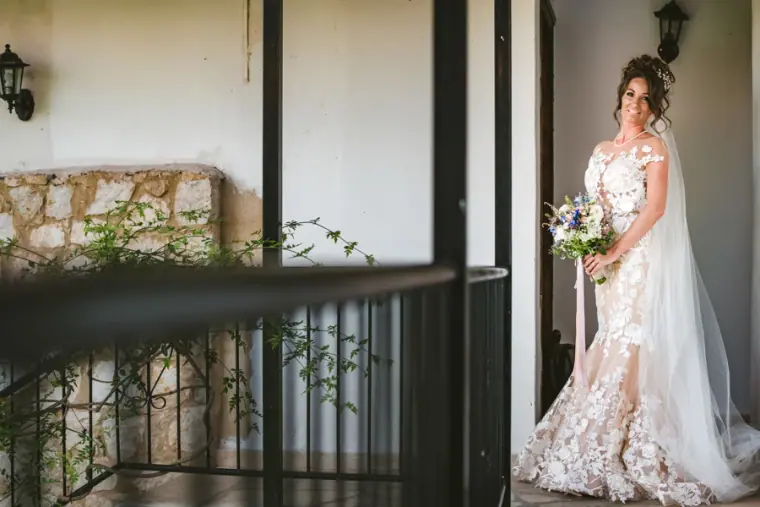 Amie in her lace gown and veil holding a bouquet on a balcony