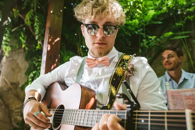 Guitarist in sunglasses and a bow tie playing acoustic guitar at the ceremony