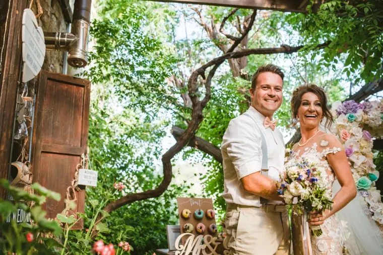 Amie and Graeme smiling beneath trees with her wildflower bouquet