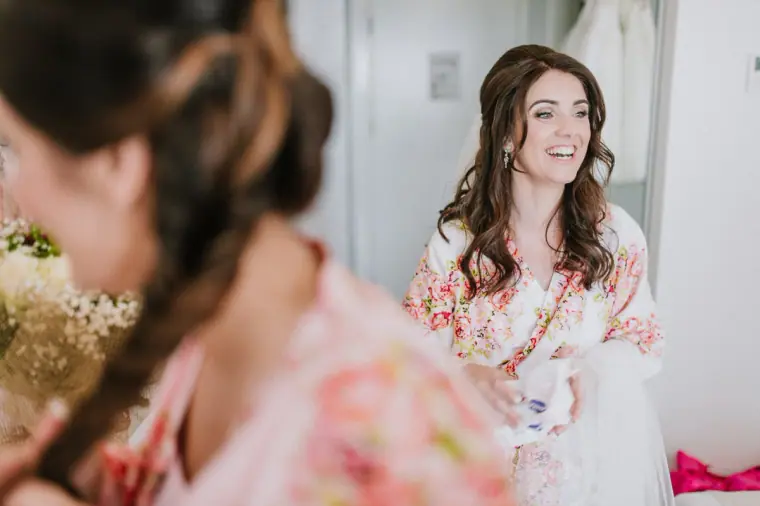 Claire laughing in her floral robe, seen past a bridesmaid's braided hair