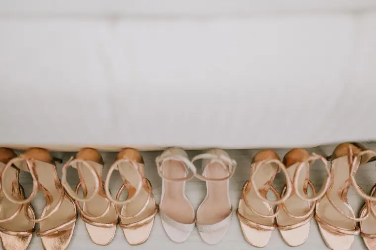 Row of rose-gold bridesmaid sandals lined up beneath a bed
