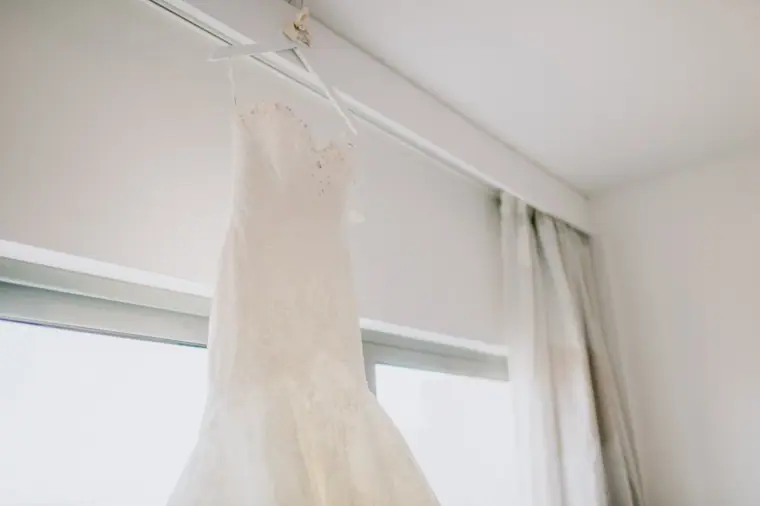 Fitted lace wedding dress hanging by a bright hotel window