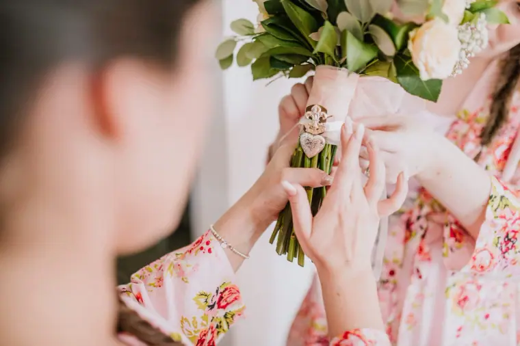 Bridesmaid's hands attaching a photo charm to the bridal bouquet