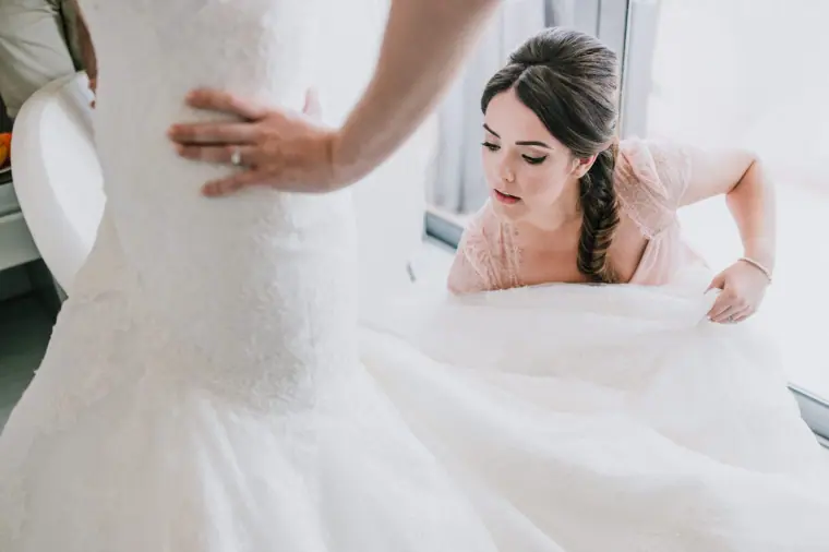 Bridesmaid arranging the train of Claire's gown in the hotel room